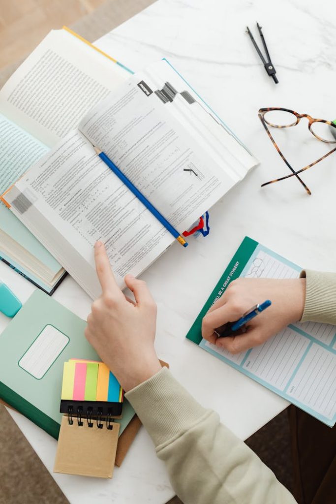 Close-up of a student studying with books and notes on a white desk.